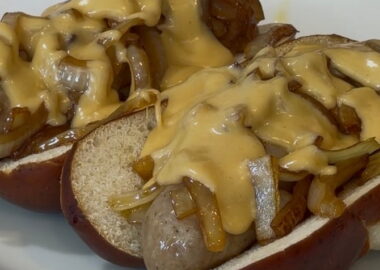 Bratwurst on a pretzel bun with onions and cheese sauce.