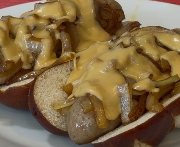 Bratwurst on a pretzel bun with onions and cheese sauce.